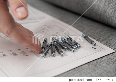 A human hand arranging metal screws and plastic dowels on a furniture assembly instruction manual, illustrating the process of do-it-yourself home renovation A human hand arranging metal screws and plastic dowels on a furniture assembly instruction manual, illustrating the process of do-it-yourself home renovation 135908605