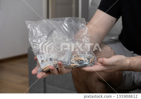 Person's hands holding a transparent plastic bag filled with essential furniture assembly hardware, symbolizing do-it-yourself projects and home setup 135908612