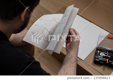 Man carefully studying a detailed furniture assembly instruction manual with diagrams, preparing for a challenging home improvement project or new living space setup 135908621