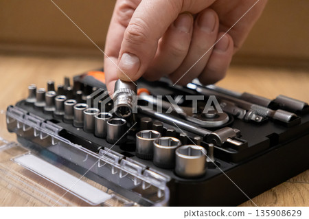 A mechanic's hand carefully selects a durable metal socket from an organized professional tool kit, emphasizing precision for crucial automotive repair and industrial maintenance A mechanic's hand carefully selects a durable metal socket from an organized professional tool kit, emphasizing precision for crucial automotive repair and industrial maintenance 135908629