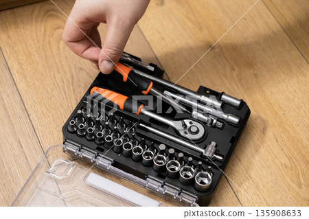 Hand opening an organized tool kit with screwdriver bits, sockets, and a ratchet, essential for versatile home repairs and DIY 135908633
