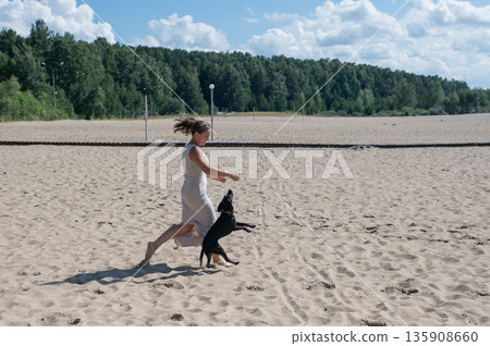 Caucasian woman walking on the beach with her dog.  135908660