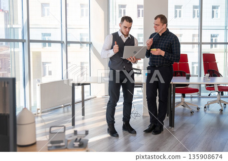 Two Caucasian men looking at a laptop and discussing work.  135908674