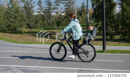 Caucasian woman rides bicycle with one-year-old son in park.  135908745
