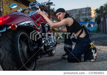 Brunette woman repairs a red motorcycle. Brunette woman repairs a red motorcycle. 135908801
