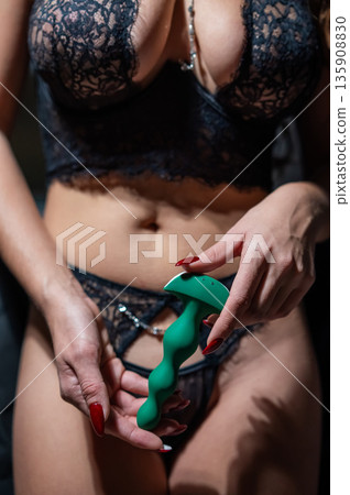 Woman in lace lingerie holding green anal beads.  135908830