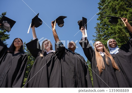 Young women of different nationalities pull graduation caps up. Young women of different nationalities pull graduation caps up. 135908889