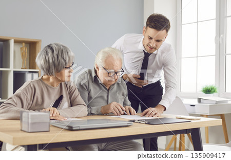 Realtor assists to sign property purchase contract for seniors family. Real estate sign contract providing support to elderly couple they embark on new chapter of life with signing contract. 135909417