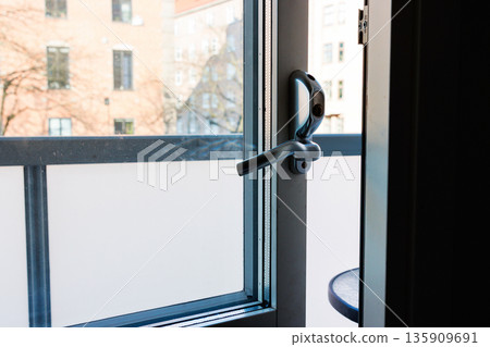 Open balcony door with handle and urban building view in daylight Open balcony door with handle and urban building view in daylight 135909691