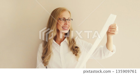 Surprised happy mature woman in glasses looking amazed at the high price tag on long paper receipt Surprised happy mature woman in glasses looking amazed at the high price tag on long paper receipt 135909761
