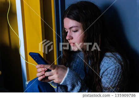 Young woman holding and using smartphone with charging cable indoors 135909786