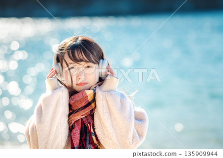 冬天，年輕女子在海邊戴著耳機聽音樂。 135909944