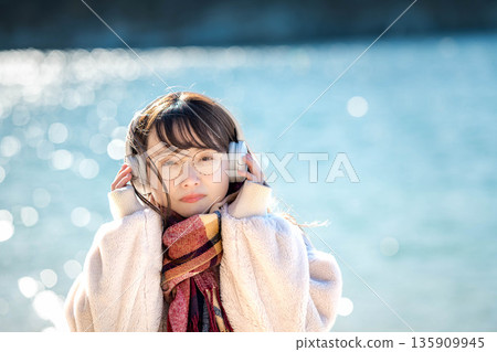 冬天，年輕女子在海邊戴著耳機聽音樂。 135909945