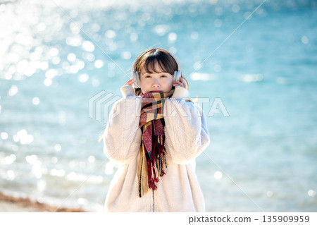 Young woman listening to music with headphones by the sea in winter Young woman listening to music with headphones by the sea in winter 135909959