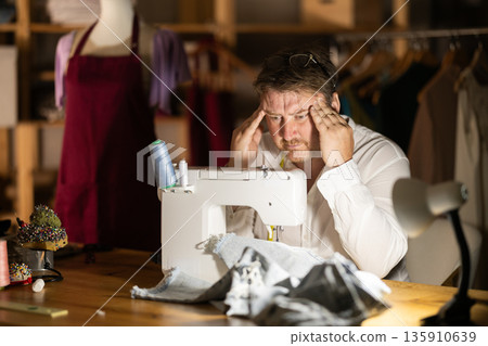 Tired male tailor rubs temples, tiring days work is behind him Tired male tailor rubs temples, tiring days work is behind him 135910639