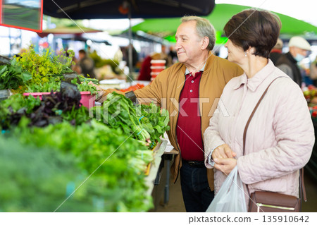 Smiling elderly male and female picking fresh organic greenery at local grocery bazaar 135910642