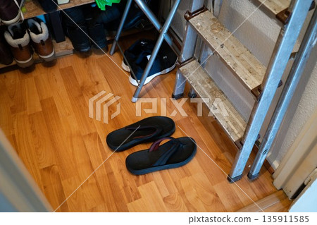 Black flip-flops stored in a wardrobe space with a step ladder nearby. Simple, everyday home organization scene. Concept of footwear, storage, home, interior, casual lifestyle. Black flip-flops stored in a wardrobe space with a step ladder nearby. Simple, everyday home organization scene. Concept of footwear, storage, home, interior, casual lifestyle. 135911585