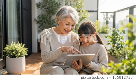 Grandmother enjoying a tablet with her grandchildren on the balcony 135912733