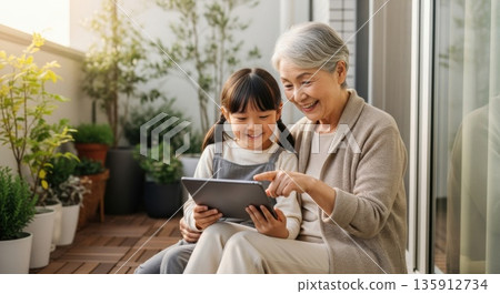 Grandmother enjoying a tablet with her grandchildren on the balcony 135912734