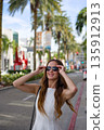 Stylish woman adjusting sunglasses on sunny city street 135912913