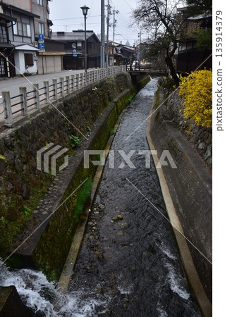 日本岐阜縣高山市的古老街景。古老的房屋散發著歷史氣息。高山春季祭典期間的清晨景象。一條小溪穿過城市。 日本岐阜縣高山市的古老街景。古老的房屋散發著歷史氣息。高山春季祭典期間的清晨景象。一條小溪穿過城市。 135914379