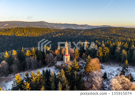 The Stepanka lookout tower stands tall amidst the trees in the Jizera Mountains during winter. Sunlight casts shadows over the landscape creating a warm glow. The Stepanka lookout tower stands tall amidst the trees in the Jizera Mountains during winter. Sunlight casts shadows over the landscape creating a warm glow. 135915074