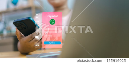 Hand holding smartphone with secure payment interface and confirmation button. Concept of mobile banking, digital transaction safety, and online shopping with protection shield icon. 135916025