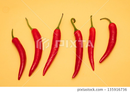 Row of red chilli peppers on yellow 135916736