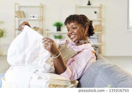 Happy African American Woman Doing Housework And Sorting Clean Laundry Happy African American Woman Doing Housework And Sorting Clean Laundry 135916793