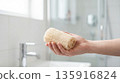 Hand holds natural loofah sponge. Loofah sponge for gentle exfoliation, loofah sponge for eco shower hygiene, for spring cleaning, earth day, self care campaigns, minimal spa concept 135916824