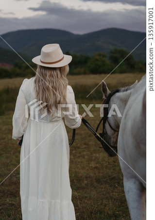 Woman walks with horse in field near mountains during evening time Woman walks with horse in field near mountains during evening time 135917001