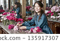 Cute smiling east asian female seller organizing pastel chrysanthemums and orchids on a marble-top counter. Serene flower boutique. Natural lighting. 135917307