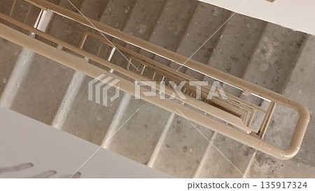 A high-angle view of a concrete stairwell featuring a metal railing, highlighting architectural design elements. This image represents urban construction and design concepts effectively. A high-angle view of a concrete stairwell featuring a metal railing, highlighting architectural design elements. This image represents urban construction and design concepts effectively. 135917324