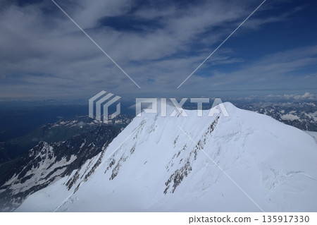 A stunning rock formation covered in snow, set against a clear blue sky with fluffy clouds in the background, creating a peaceful and breathtaking mountain landscape. A stunning rock formation covered in snow, set against a clear blue sky with fluffy clouds in the background, creating a peaceful and breathtaking mountain landscape. 135917330
