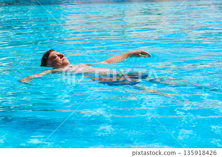 Adult Man Floating on His Back in the Pool of an Egyptian Hotel, Enjoying a Relaxing Day Under the Sun in a Tropical Paradise Adult Man Floating on His Back in the Pool of an Egyptian Hotel, Enjoying a Relaxing Day Under the Sun in a Tropical Paradise 135918426