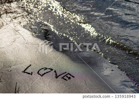 Love word handwritten on wet beach sand with gentle sea water creating romantic mood and emotional natural background 135918943