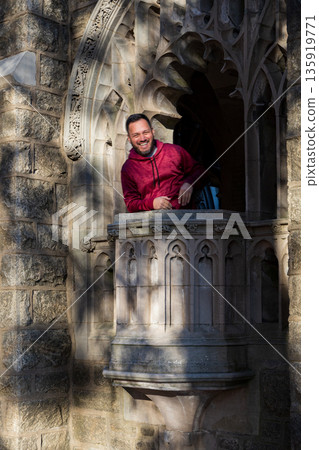 A man in a red jacket is standing on a balcony of a building 135919771