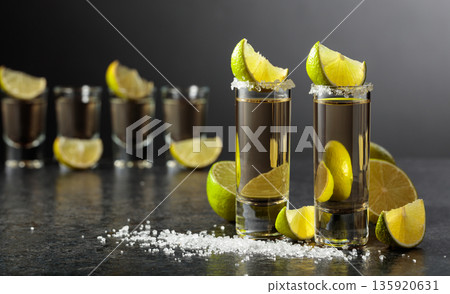 Tequila shots with salt and lime slices on a black stone table. Tequila shots with salt and lime slices on a black stone table. 135920631