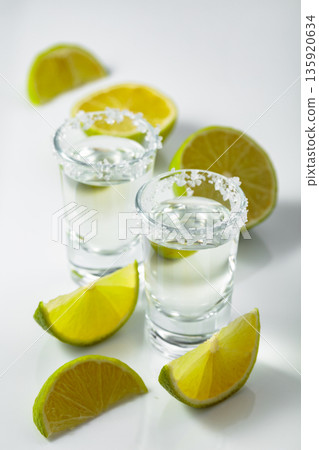 Tequila with salt and lime slices on a white table. Tequila with salt and lime slices on a white table. 135920634