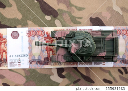 Russian rubles money bills and tank on camouflage fabric close up. Concept of russian army funds and heavy weaponry or machinery Russian rubles money bills and tank on camouflage fabric close up. Concept of russian army funds and heavy weaponry or machinery 135921683
