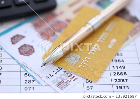 Credit card and pen with russian ruble currency money bills banknotes on calculations document background. Business, financial operations and accounting in Russian Federation 135921687