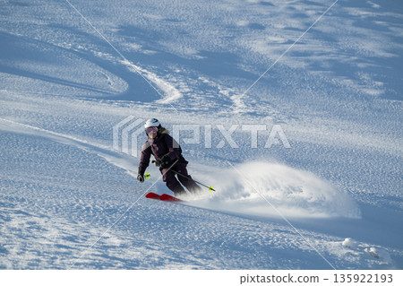 Skier carving powder on a sunny mountainside, off-piste freeride action in fresh snow during winter adventure 135922193