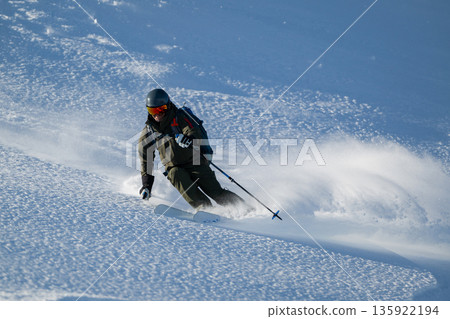 Skier carving through fresh powder on a snowy slope with protective gear and dynamic stance 135922194