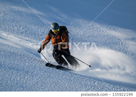 Skier carving a high-speed line down a snowy mountain slope in fresh backcountry powder Skier carving a high-speed line down a snowy mountain slope in fresh backcountry powder 135922199