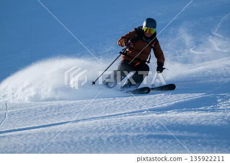 Skier carving through fresh powder on a bright mountain slope 135922211