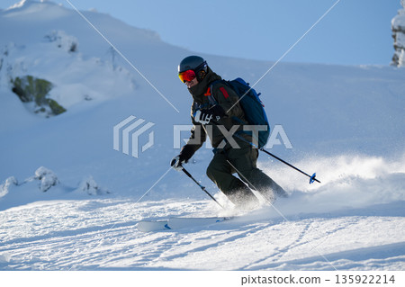Skier in rugged backcountry gear carving a turn on fresh powder in the mountains 135922214