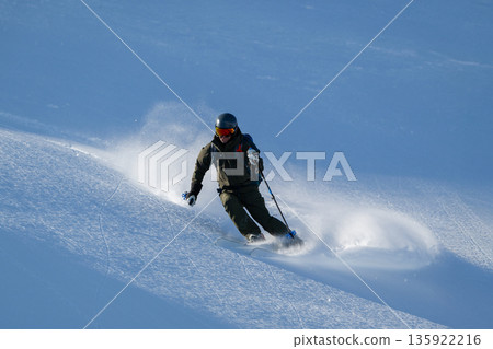Skier carving a turn on a snowy mountain slope, mastering off-piste freeride technique 135922216