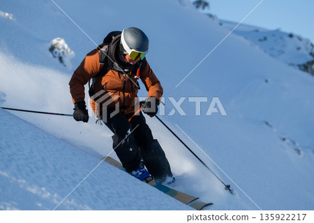 Skier in orange jacket carving down fresh powder on a snowy mountain slope, action and adventure 135922217