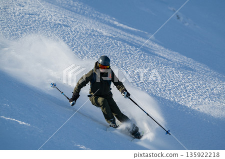 Skier carving through fresh powder on a steep off-piste slope under bright daylight 135922218