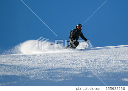 Skier carving a turn on fresh powder under a clear blue sky in the mountains 135922238
